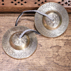 Tibetan Tingsha Bells – Handcrafted pair with lotus dome engraving and leather strap on rustic wood, meditation cymbals