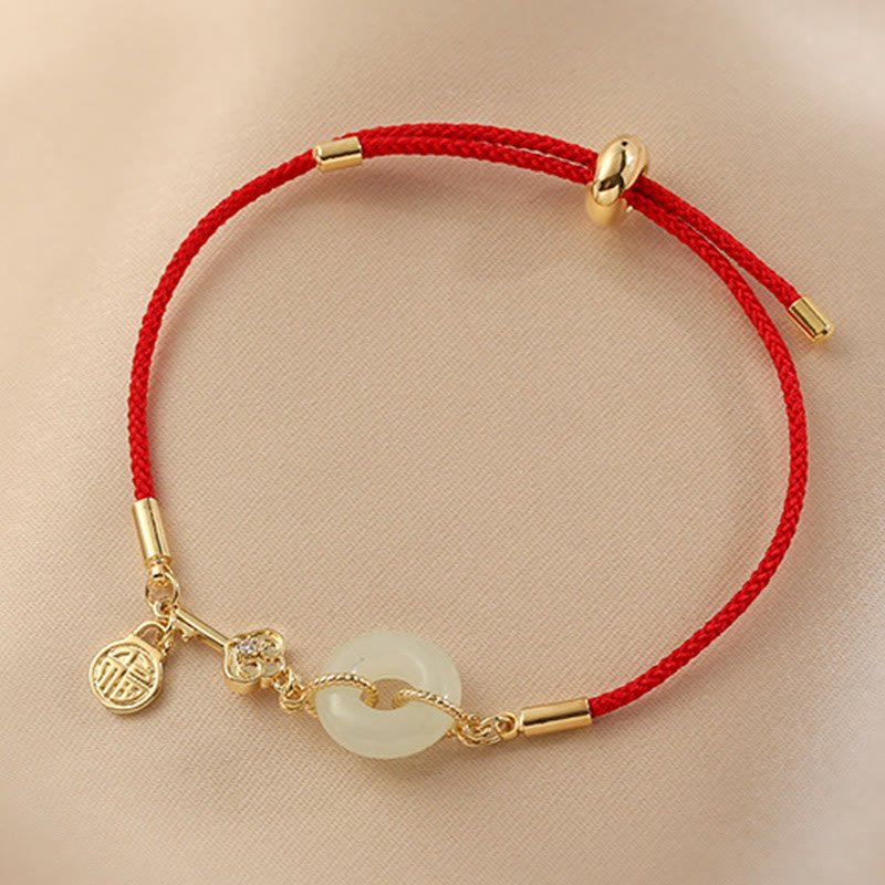 Adjustable red cord bracelet with white jade ping an kou disc, gold fortune charm with Fu character and crystal accent on beige fabric background