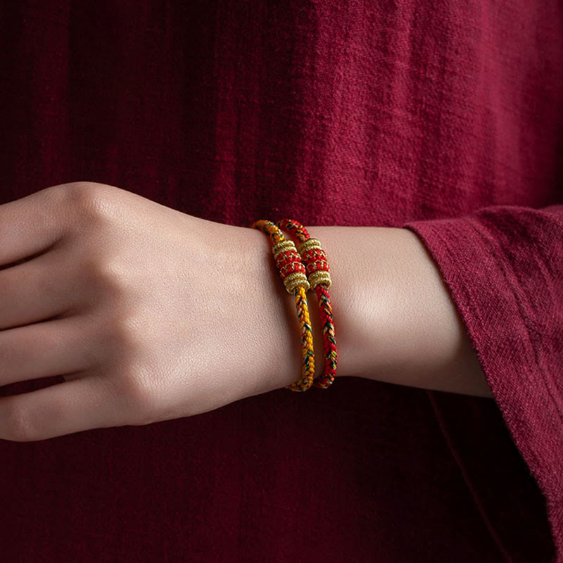 Stacked handmade Chinese lucky red string bracelets with gold knot detailing on woman's wrist, traditional woven cord protection jewelry for women