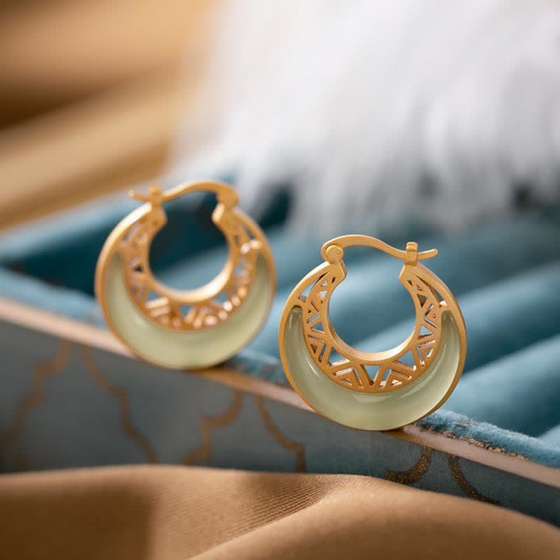 Crescent Moon Jade Drop Earrings – Gold double-ring hoop earrings with white jade inlay, geometric lattice cutouts on cream box with green satin ribbon, low angle