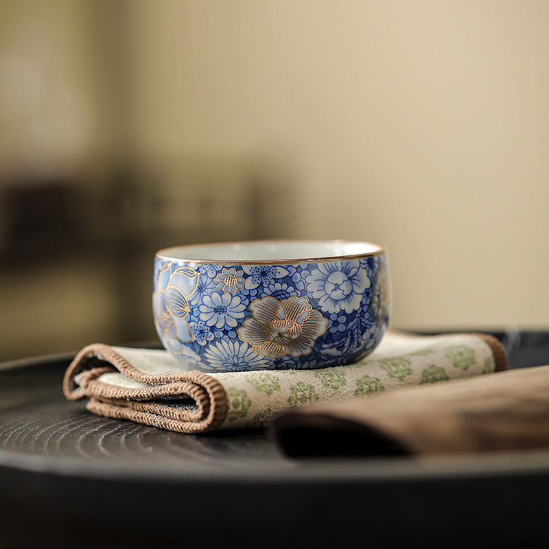 Lotus Chrysanthemum Ceramic Tea Cup - Blue-white floral with gold rim on fabric mat, ceremonial