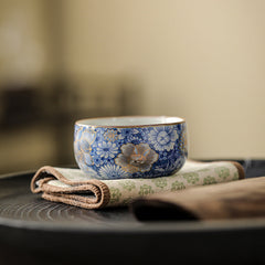 Lotus Chrysanthemum Ceramic Tea Cup - Blue-white floral with gold rim on fabric mat, ceremonial