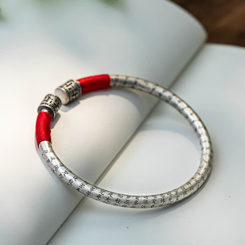 Tibetan Red String Bracelet – bangle on open book with greenery, engraved silver with red cord