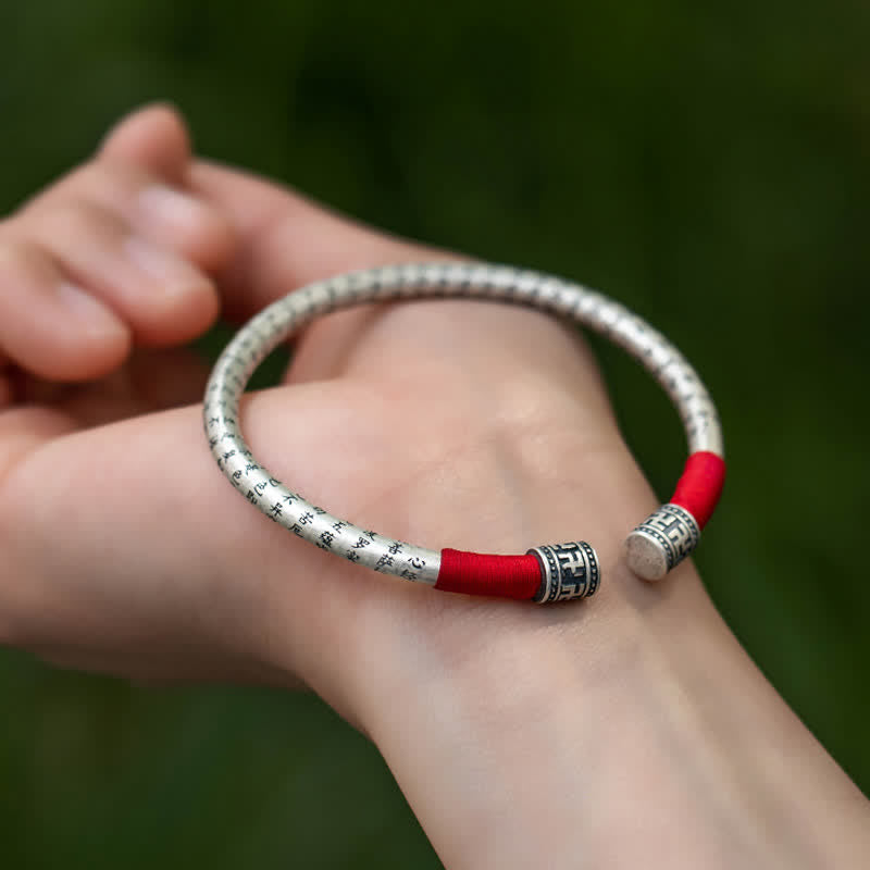 Tibetan Red String Bracelet – worn on wrist with natural green bokeh, sutra-engraved silver cuff