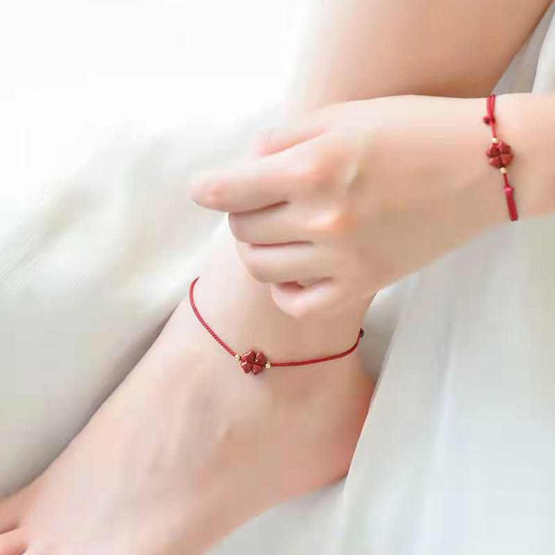 Red cord bracelet with cinnabar four leaf clover carved charm gold-tone beads and adjustable sliding knot on red textured surface with blurred traditional architectural background