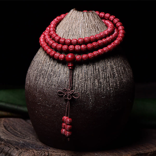 108 Mala Beads Cinnabar Bracelet – Draped display with green foliage, carved bead mala
