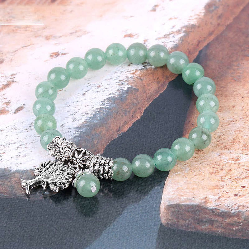Tree of Life aventurine bracelet with pale green quartz beads, ornate silver Tree of Life pendant with branch and root motifs on weathered wood.