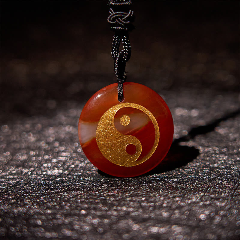 Yin Yang Crystal Necklace – Red-brown carnelian pendant with gold yin-yang symbol on polished natural stone, black braided co