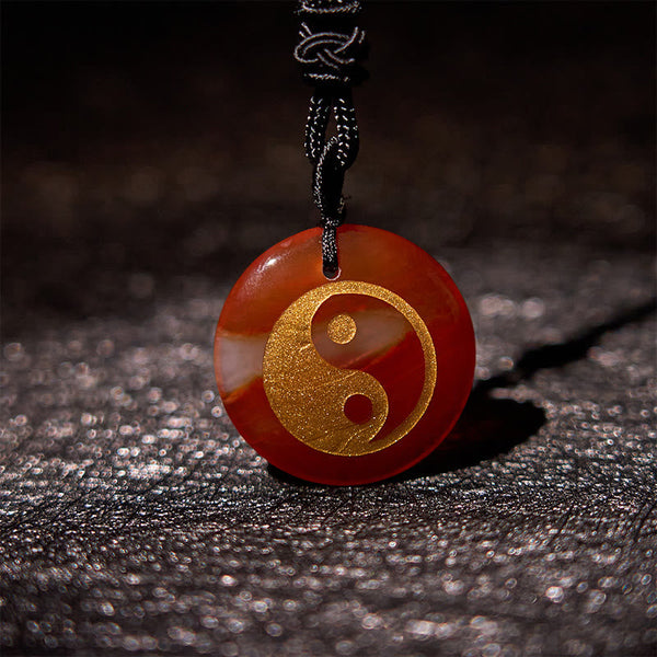 Yin Yang Crystal Necklace – Red-brown carnelian pendant with gold yin-yang symbol on polished natural stone, black braided co