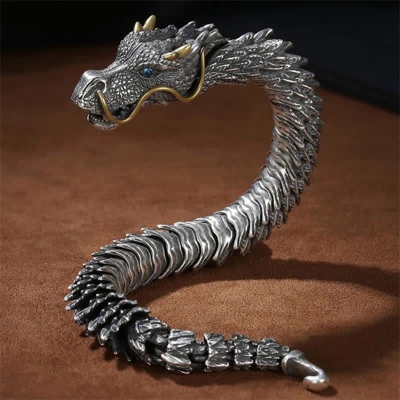 Dragon scale bracelet on warm brown leather background with oxidized silver body blue sapphire eye gold accents and articulated segmented construction