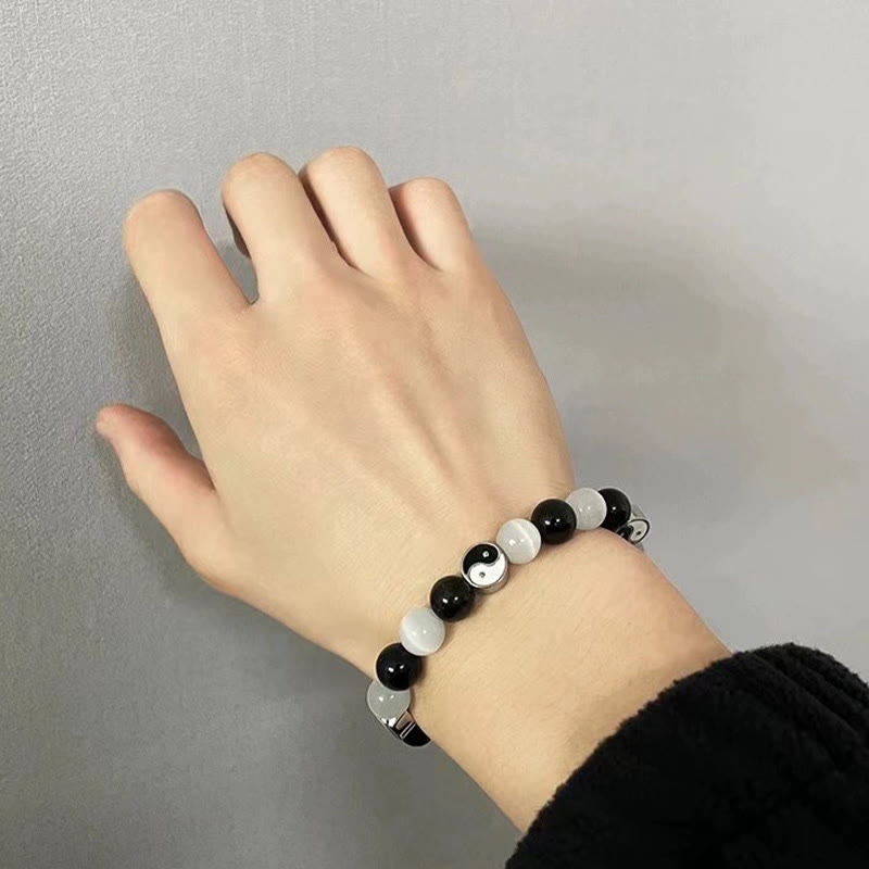 Black Obsidian Cat Eye Yin Yang Bracelet - worn on hand on gray surface, black obsidian yin-yang bracelet on wrist