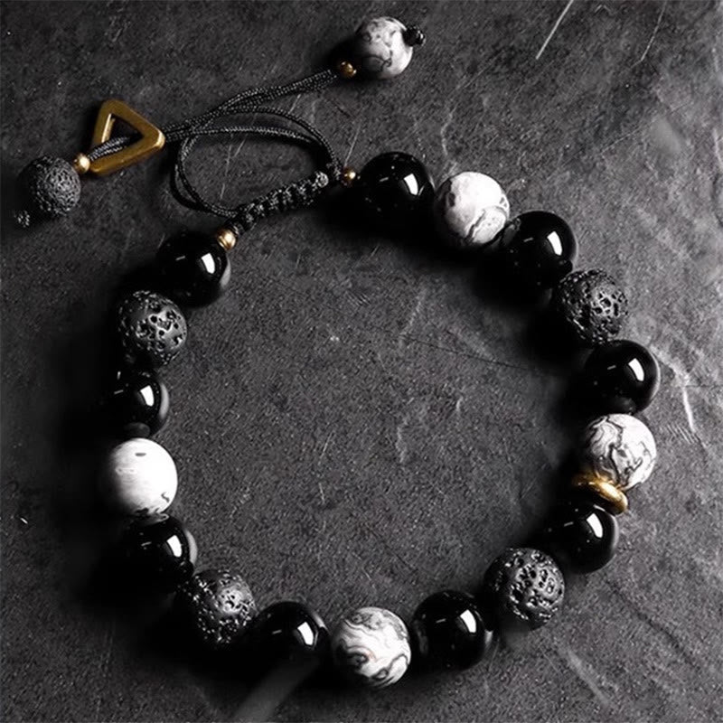 Black Obsidian Lava Rock Yin Yang Bracelet - top-down flat lay on dark slate, gold triangular toggle clasp visible