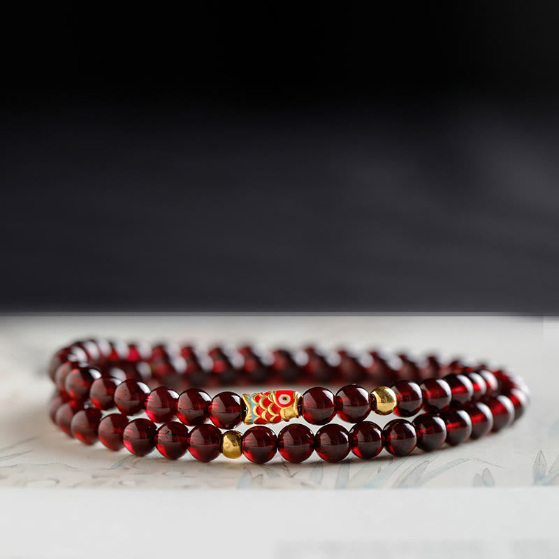 999 Gold Koi Fish Bracelet – top-down view on white cloth, 999 gold chain, natural garnet beads
