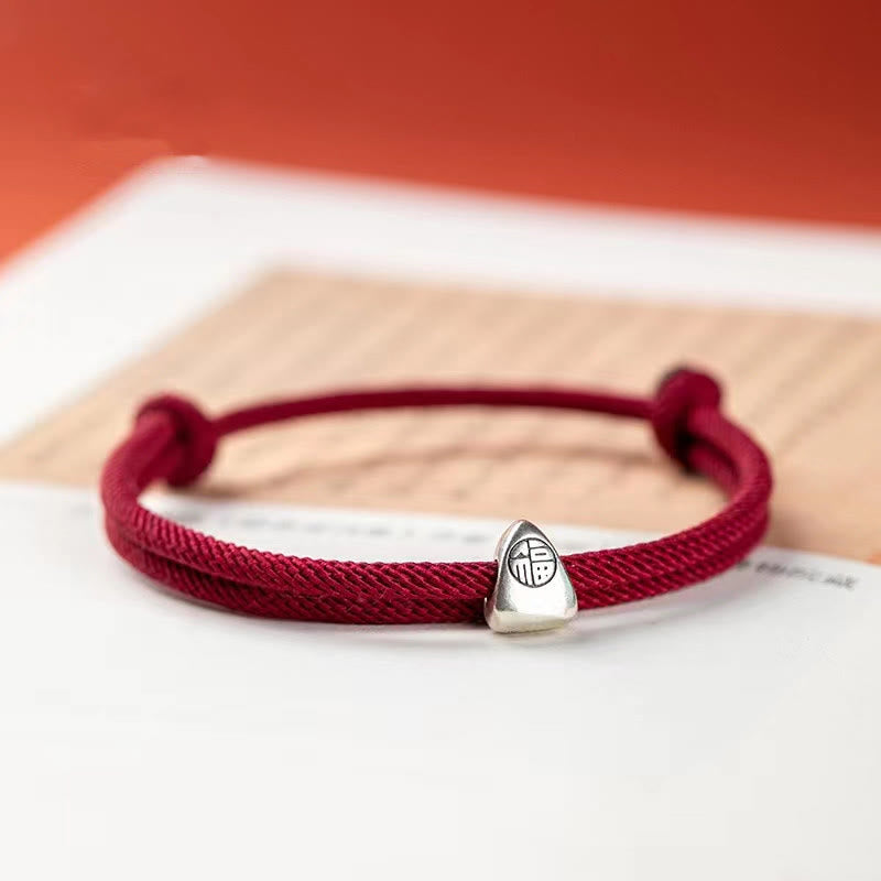 925 Silver Fu Character Braided Bracelet – Burgundy cord bracelet with silver fortune charm held by hand against dark backdrop, three-quarter lifestyle close-up