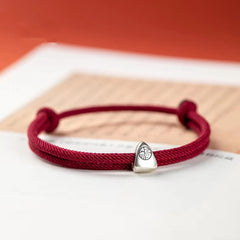 925 Silver Fu Character Braided Bracelet – Burgundy cord bracelet with silver fortune charm held by hand against dark backdrop, three-quarter lifestyle close-up