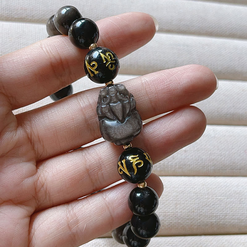 Silver Sheen & Black Obsidian PiXiu Bracelet – close-up of carved Pixiu figure and gold Sanskrit beads on hand, obsidian h...