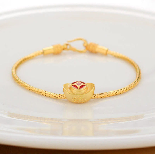 18K Gold Om Mani Padme Hum Koi Fish Bracelet – gold ingot yuanbao charm with red enamel on braided chain, white dish, elevated front view