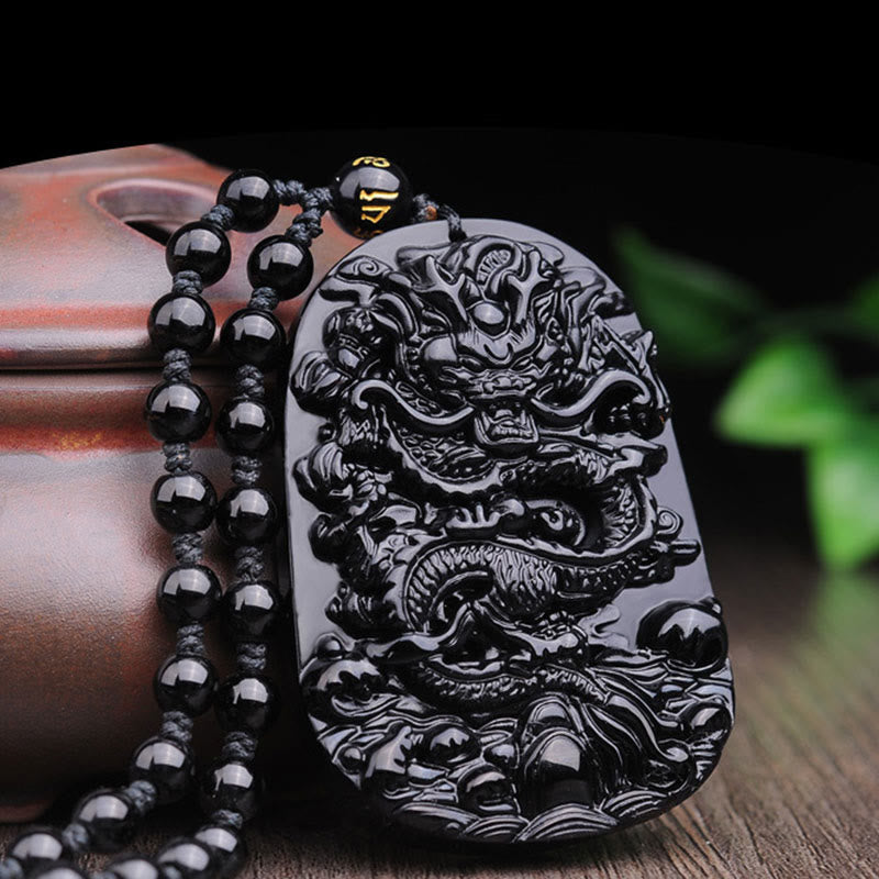 Black Obsidian Dragon Pendant – Relief dragon detail on dark wood with green foliage, feng shui