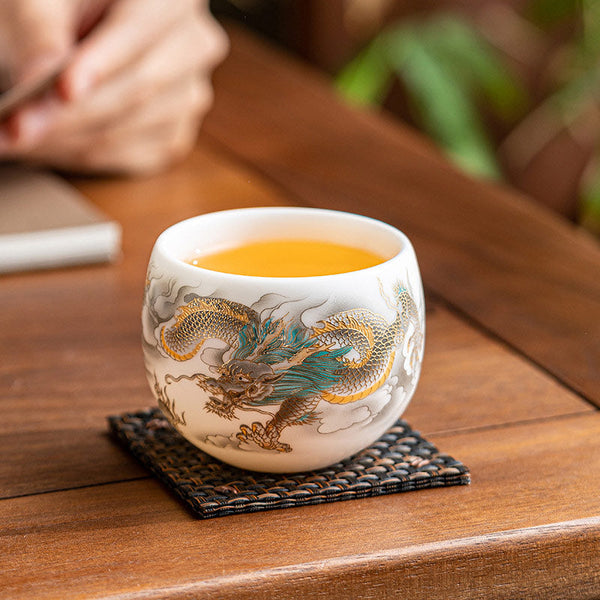 Dragon Phoenix Clouds Ceramic Teacup Gift Set – Gold and teal dragon cup with amber tea on woven coaster, lifestyle