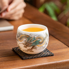 Dragon Phoenix Clouds Ceramic Teacup Gift Set – Gold and teal dragon cup with amber tea on woven coaster, lifestyle