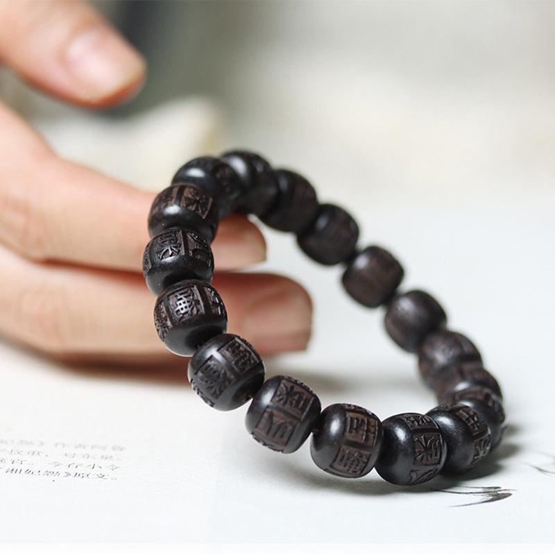 Ebony Wood Mantra Bracelet – Hand supporting beads on white surface showing carved texture, wooden mala