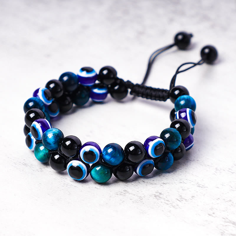 Evil Eye Hematite Tiger Eye Bracelet – teal cat's eye and black beads with evil eye motifs on gray surface