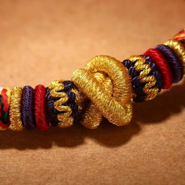 Tibetan Mantra Bracelet – Macro close-up of gold metallic knot with red and purple cord bands, knot detail