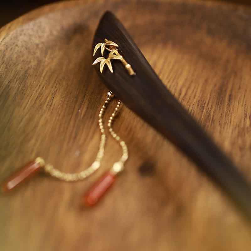 Close-up of ebony wood hairpin with gold bamboo decoration and red agate tassels on wood surface