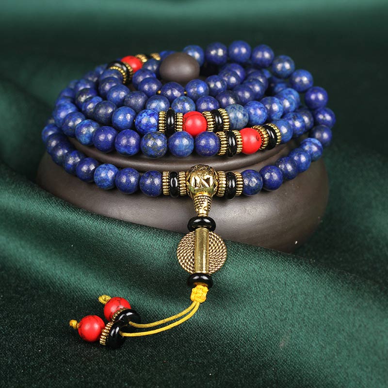 Lapis Lazuli Red Turquoise Tibetan Mala Bracelet coiled on wooden stand, 108 deep blue lapis beads with gold pyrite flecks, red coral marker beads, ornate gold guru bead with yellow tassel, green velvet background