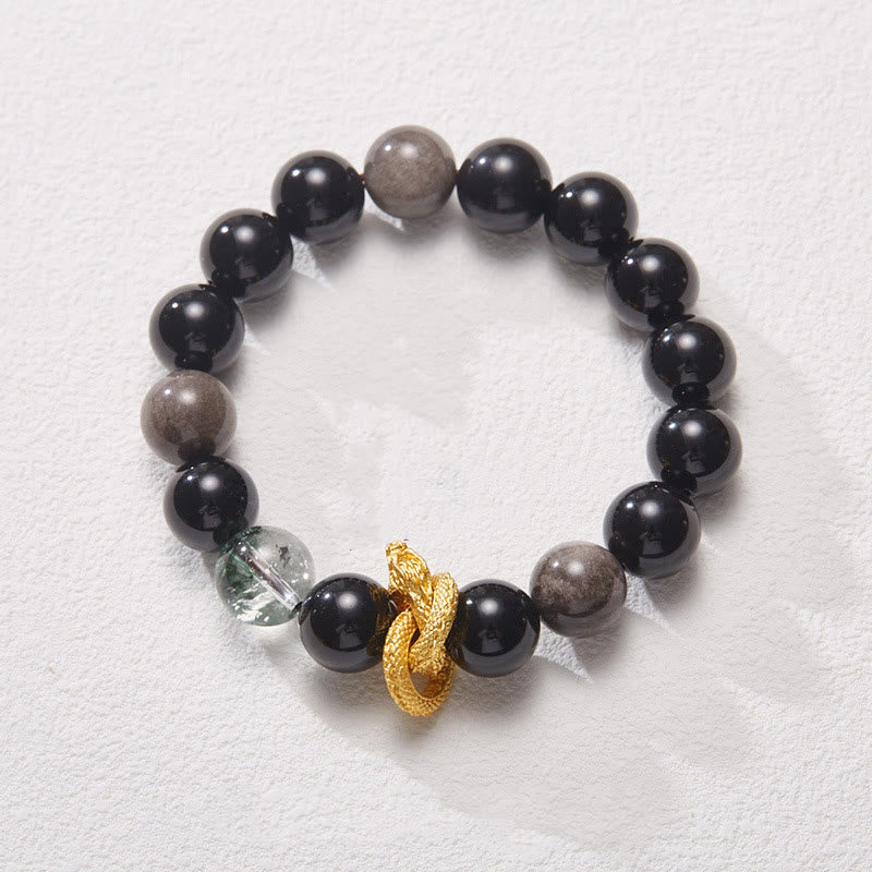 Silver Sheen Obsidian Dragon Bracelet – Angled view on textured surface with gray beads, dragon charm, transformative