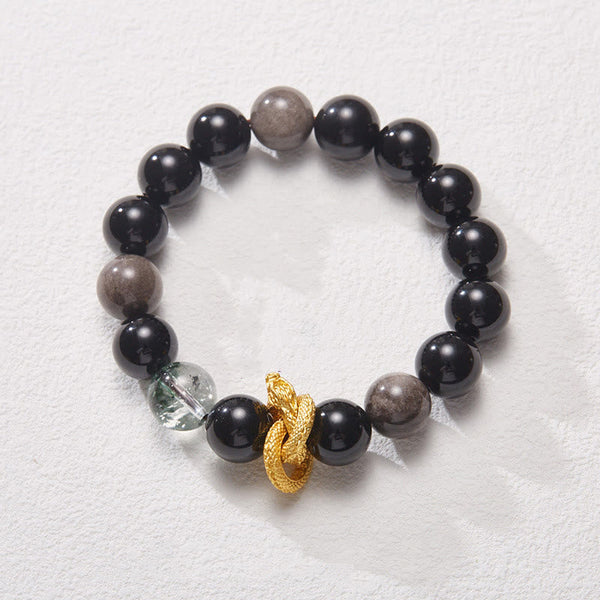 Silver Sheen Obsidian Dragon Bracelet – Angled view on textured surface with gray beads, dragon charm, transformative