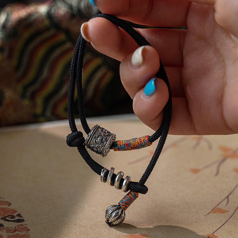 Tibetan Om Mani Padme Hum Wrap Bracelet – Worn on wrist with silver mantra cylinder and fish-tail charm, gray denim sleeve lifestyle photo