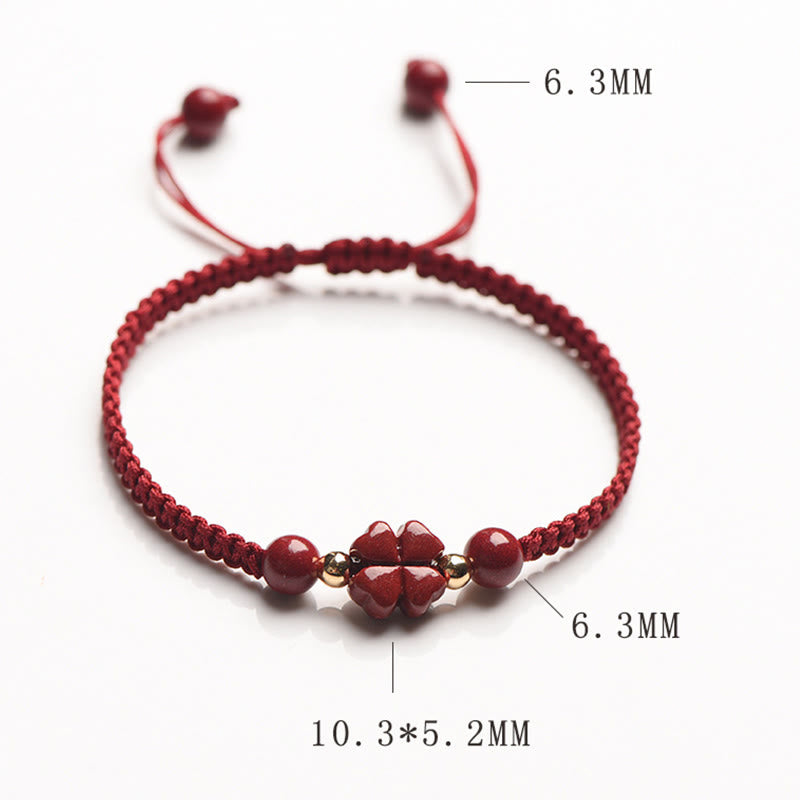 Adjustable red macrame bracelet with four-leaf clover charm and round cinnabar beads on white background, top-down product photography with dimension annotations