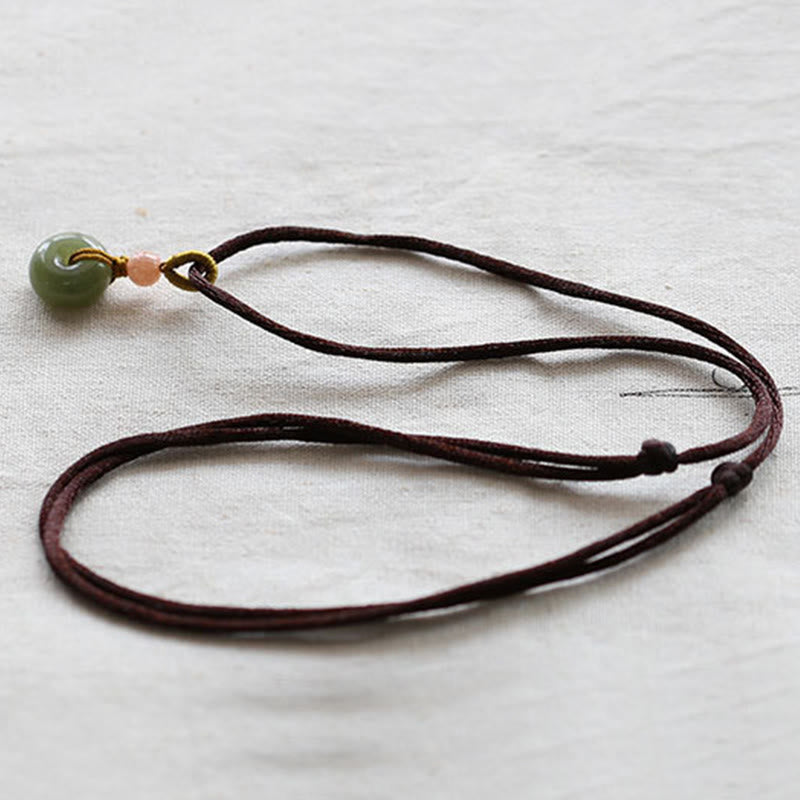 Jade Peace Buckle Lotus Necklace – Flat lay of jade donut on brown cord with adjustable knots on cream linen, jade necklace