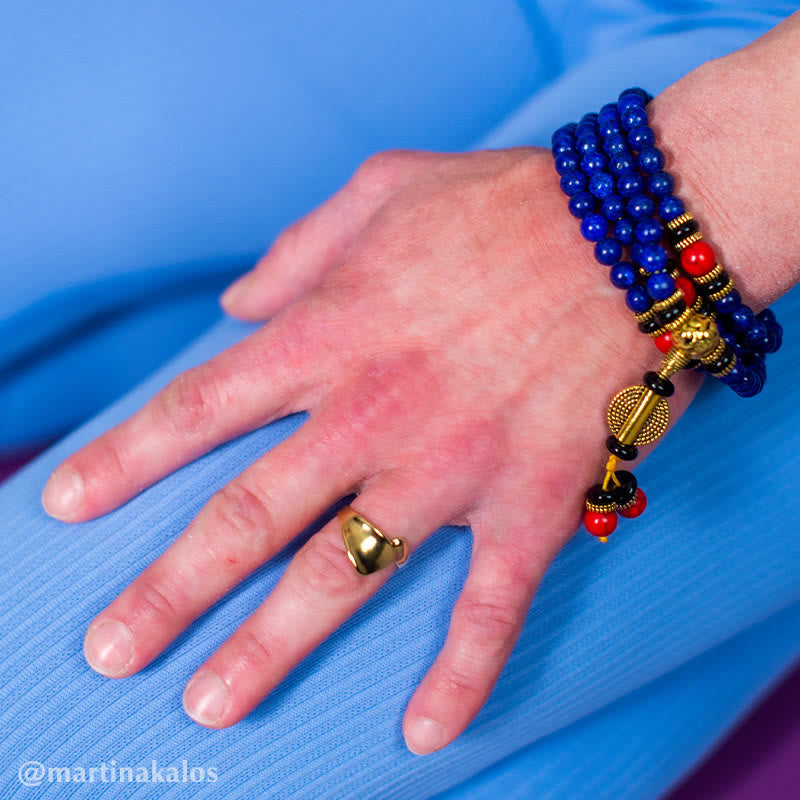Lapis Lazuli Red Turquoise Tibetan Mala Bracelet worn on wrist, 108 deep blue beads with red coral and black accents, gold Buddha head charm, mandala prayer wheel pendant, gold ring, model lifestyle shot