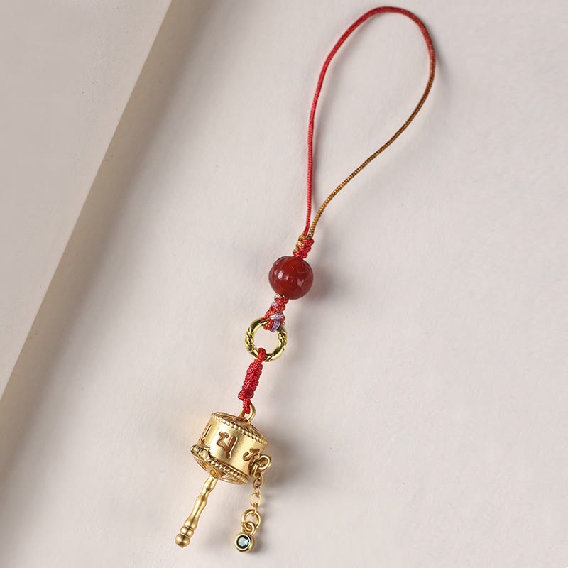 Prayer Wheel Phone Charm – Diagonal overhead shot on off-white, gold prayer wheel pendant