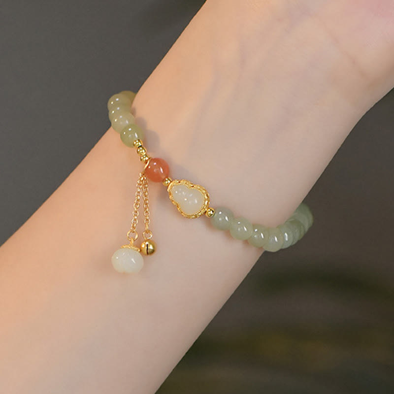 Jade Gourd Lotus Bracelet on wrist close-up with gold dangle tassel charm, warm neutral background, delicate