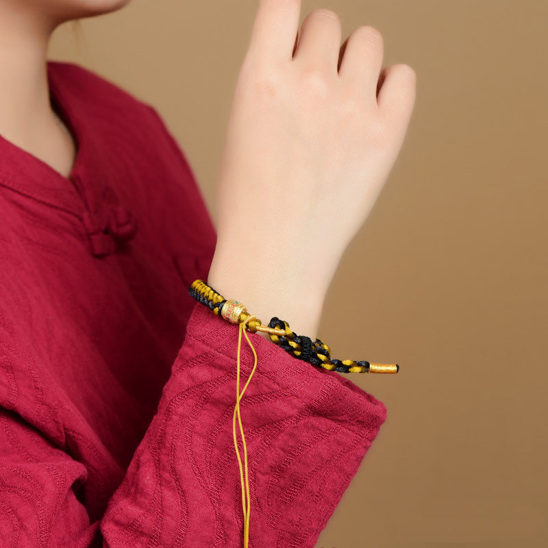 Tibetan Black Gold Dragon Scale Bracelet – worn on wrist with traditional burgundy garment, braided cord on skin
