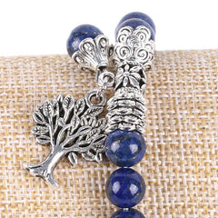 Tree of Life lapis lazuli bracelet with royal blue spherical beads and golden flecks, silver filigree caps, tree of life pendant on burlap.