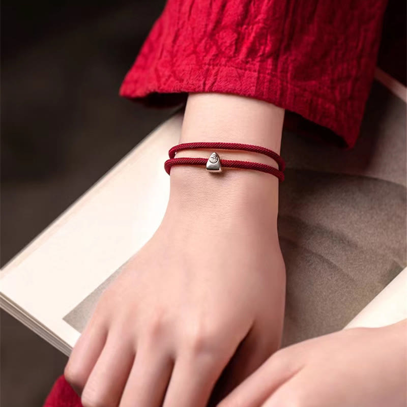 925 Silver Fu Character Braided Bracelet – Red cord bracelet with silver smiley face charm worn on wrist with open book and dark blurred background, lifestyle shot