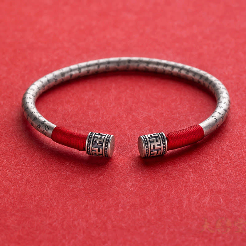 Tibetan Red String Bracelet – flat lay on red background, silver cuff with red cord and geometric caps