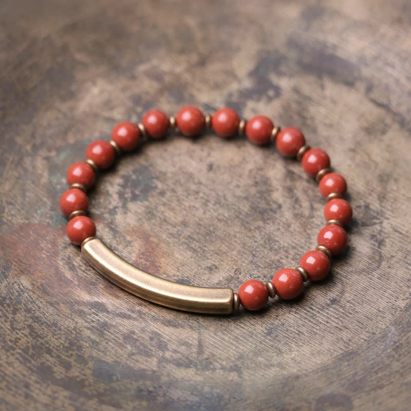 Red jasper bracelet with brass bar on weathered wood surface, terracotta round beads with antique bronze focal tube and disc spacers, rustic product photography