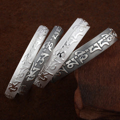 Set of four Tibetan Om Mani Padme Hum silver prayer bangles with raised Tibetan script, textured background, and ornamental end motifs.