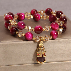 Tiger Eye Pixiu Fox Money Bag Bracelet - double-strand magenta tiger eye beaded bracelet with gold crystal spacers and central gold Pixiu wealth charm, chatoyant burgundy gemstones on satin display