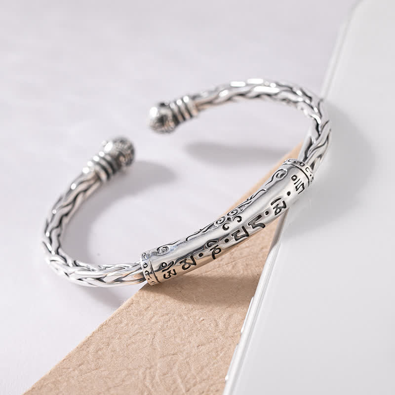 Tibetan inspired silver open cuff bracelet with twisted braided band Buddhist mantra engraved central cylinder spherical terminal finials and oxidized finish