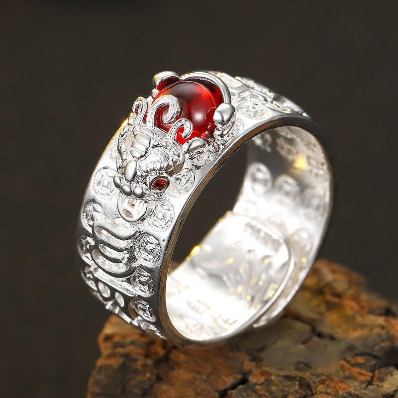 PiXiu Garnet Heart Sutra Ring – Silver foo dog ring with red gemstone worn on middle finger, warm brown leather blurred background, lifestyle close-up