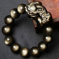 Golden Obsidian Bracelet – Close-up on dark surface with book corner, detailed PiXiu carving