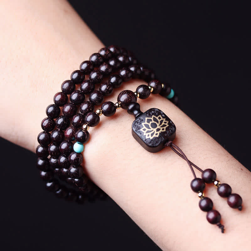 Multi-wrap 108 bead red sandalwood mala bracelet worn on wrist with turquoise accent beads and carved lotus flower guru bead against pure black background