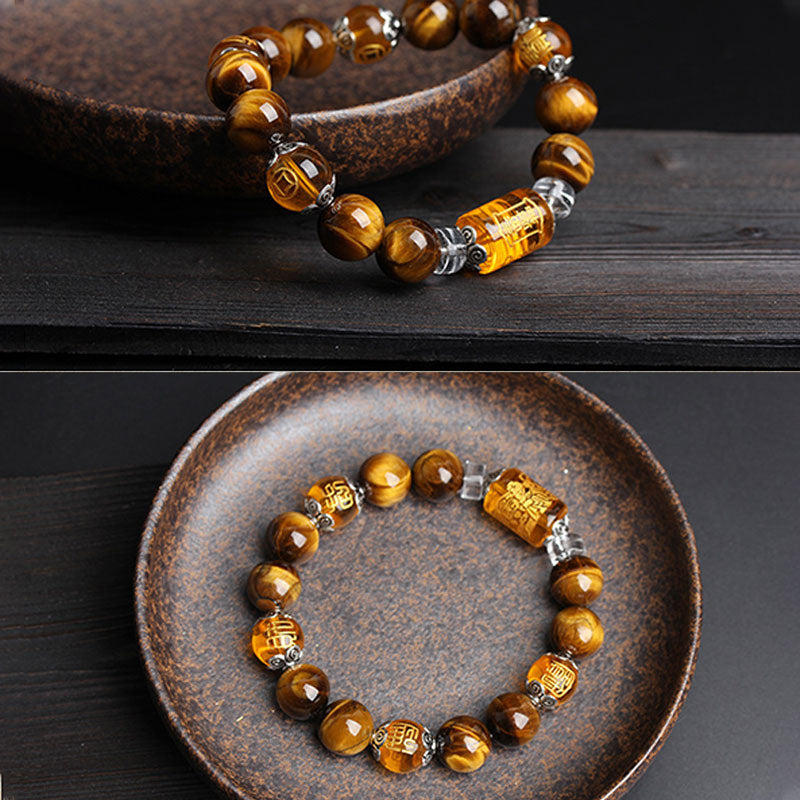 Tiger eye bracelet with carved amber fortune and longevity character beads, silver ornamental spacers and crystal dividers in brown ceramic dish on dark wood