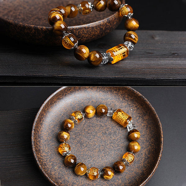 Tiger eye bracelet with carved amber fortune and longevity character beads, silver ornamental spacers and crystal dividers in brown ceramic dish on dark wood